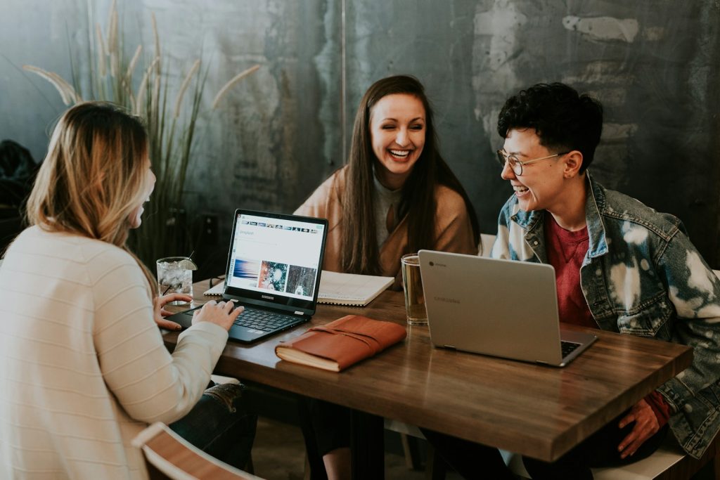 Three people collaborating happily with laptops at a wooden table in a cosy workspace