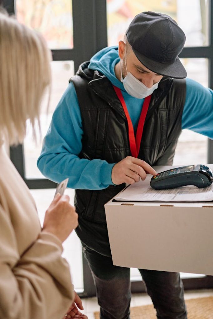 Delivery worker in mask processes contactless payment indoors with customer